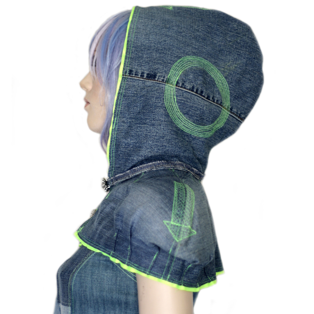 Side view of a person wearing a denim cape with hood with neon green circular and arrow stitching